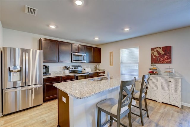 kitchen with a kitchen bar, stainless steel appliances, light hardwood / wood-style floors, light stone counters, and sink