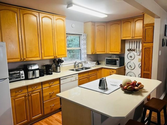 kitchen with a kitchen bar, light hardwood / wood-style floors, a center island, sink, and white appliances