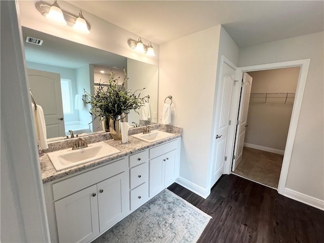 full bath featuring visible vents, a sink, wood finished floors, double vanity, and baseboards