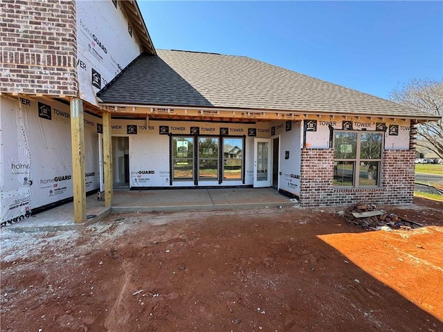 rear view of house featuring brick siding and roof with shingles