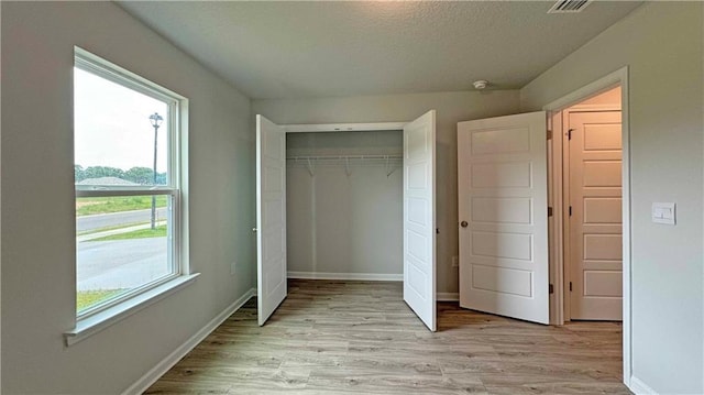 unfurnished bedroom with a textured ceiling, light wood-type flooring, multiple windows, and a closet