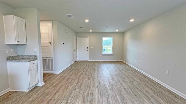 kitchen featuring white cabinets, light wood-type flooring, and light stone countertops