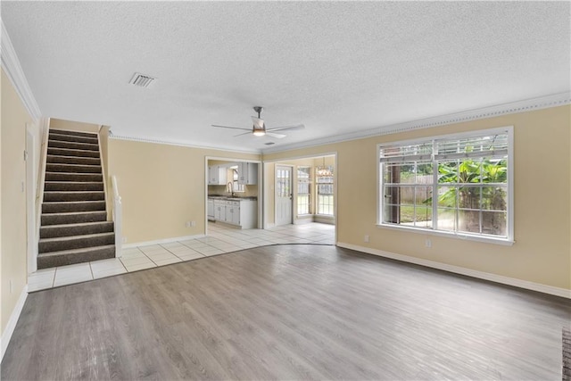 unfurnished living room featuring sink, ceiling fan, a textured ceiling, light hardwood / wood-style flooring, and crown molding