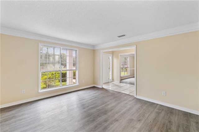 spare room featuring a wealth of natural light, a textured ceiling, ornamental molding, and light hardwood / wood-style flooring