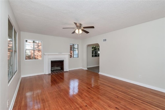 unfurnished living room with arched walkways, a fireplace, visible vents, a ceiling fan, and wood finished floors