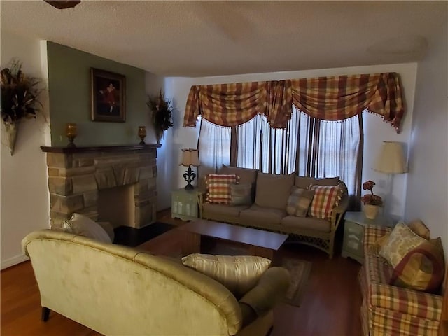 living room with a textured ceiling, hardwood / wood-style flooring, and a stone fireplace