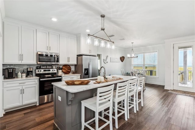 kitchen with a kitchen island with sink, hanging light fixtures, white cabinetry, and appliances with stainless steel finishes