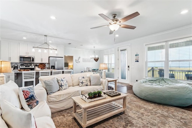 living room with crown molding, ceiling fan with notable chandelier, and light wood-type flooring