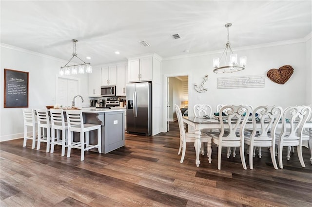 kitchen featuring stainless steel appliances, white cabinetry, pendant lighting, and a center island with sink