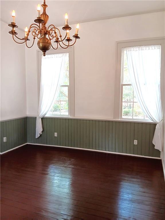 spare room with dark hardwood / wood-style flooring, a chandelier, and wood walls