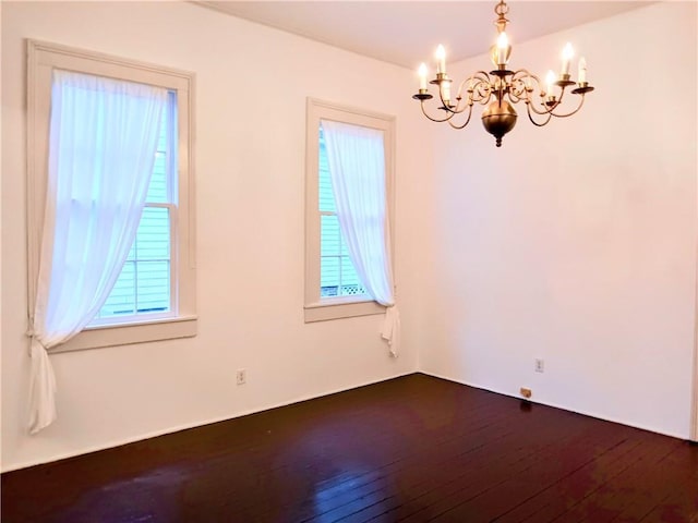 unfurnished room featuring dark wood-type flooring, plenty of natural light, and a notable chandelier