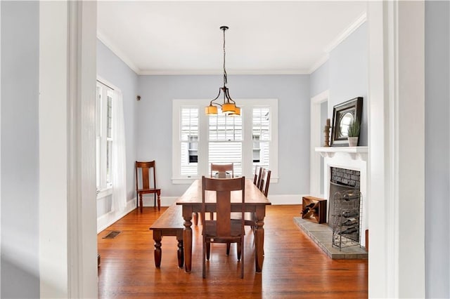 dining room featuring baseboards, visible vents, a fireplace with raised hearth, ornamental molding, and wood finished floors