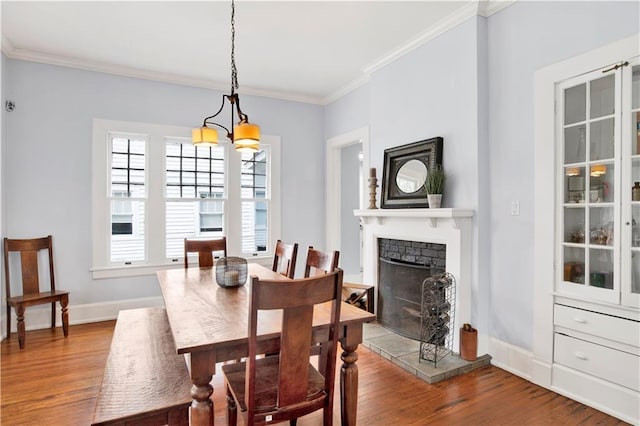 dining room featuring crown molding, baseboards, a fireplace with raised hearth, and wood finished floors