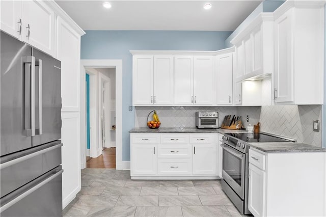 kitchen featuring backsplash, white cabinetry, stainless steel appliances, and dark stone countertops