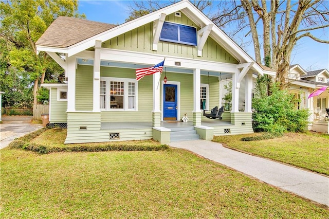 view of front facade with board and batten siding, a front yard, covered porch, and crawl space