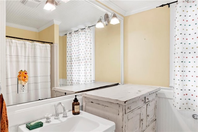 bathroom with a wainscoted wall, visible vents, crown molding, and a sink