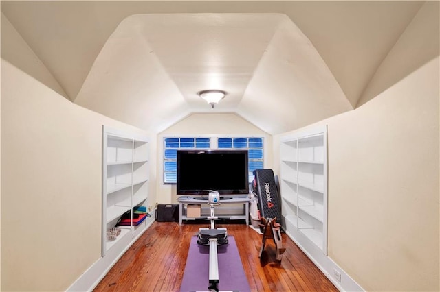 exercise room with vaulted ceiling, hardwood / wood-style floors, baseboards, and built in features