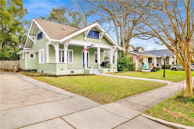 view of front of property with a shingled roof, covered porch, board and batten siding, fence, and a front lawn