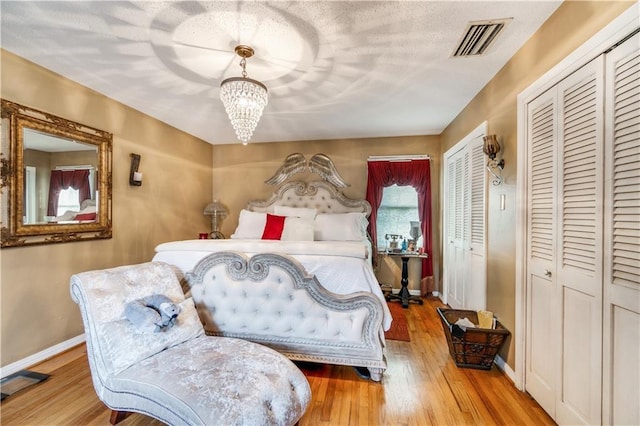 bedroom featuring two closets, an inviting chandelier, and light hardwood / wood-style flooring