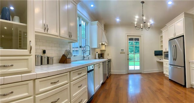 kitchen with sink, dark wood-type flooring, hanging light fixtures, appliances with stainless steel finishes, and white cabinets