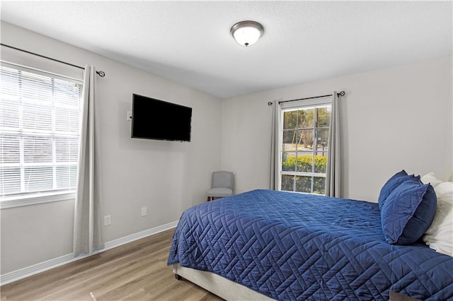 bedroom with baseboards, light wood-type flooring, and a textured ceiling