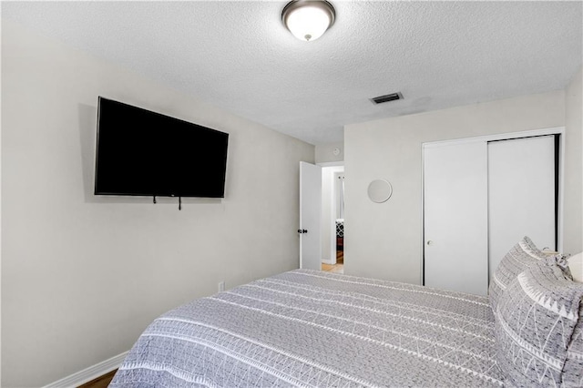 bedroom with visible vents, baseboards, a textured ceiling, and a closet