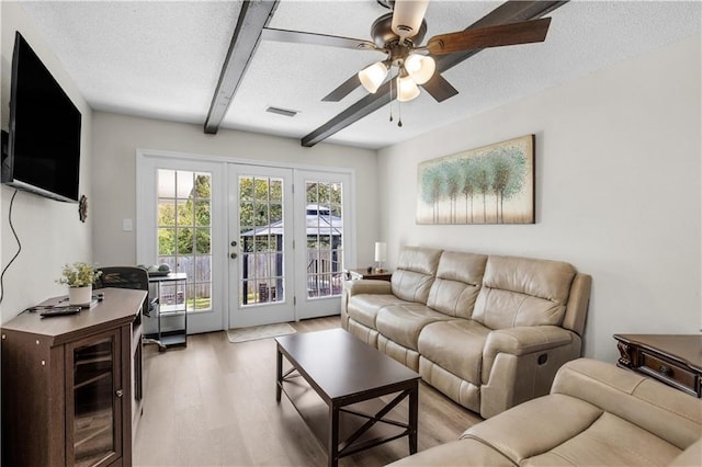 living area featuring beamed ceiling, visible vents, light wood-style flooring, a textured ceiling, and ceiling fan