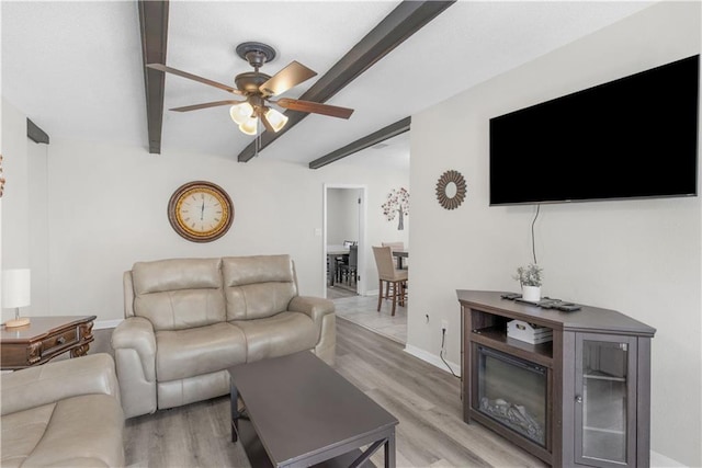 living room with beamed ceiling, baseboards, light wood-style flooring, and a ceiling fan