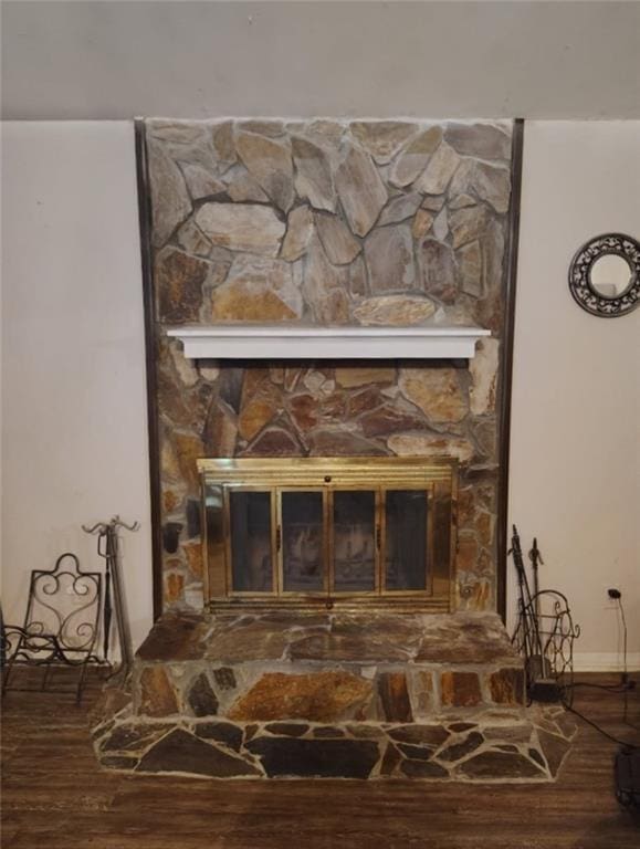 interior details featuring baseboards, a stone fireplace, and wood finished floors