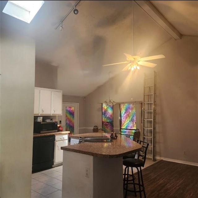 kitchen featuring stainless steel microwave, lofted ceiling with skylight, dishwasher, a kitchen breakfast bar, and white cabinetry