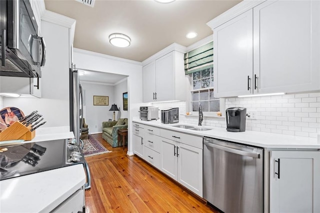 kitchen with white cabinetry, ornamental molding, light wood-type flooring, appliances with stainless steel finishes, and sink