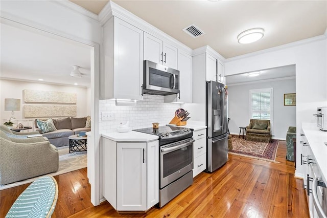 kitchen with ornamental molding, light hardwood / wood-style flooring, appliances with stainless steel finishes, white cabinets, and tasteful backsplash