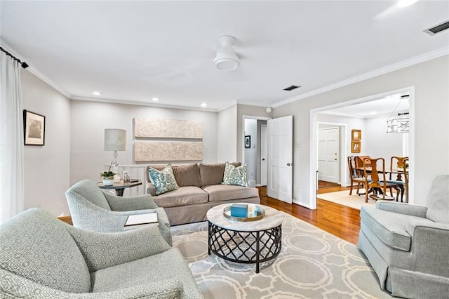 living room featuring wood-type flooring, ornamental molding, and ceiling fan with notable chandelier