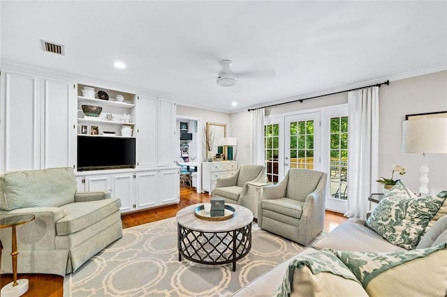 living room featuring wood-type flooring, built in shelves, ornamental molding, and ceiling fan