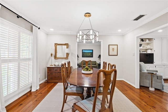 dining space with a notable chandelier, built in features, ornamental molding, and hardwood / wood-style flooring