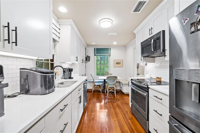 kitchen with white cabinetry, appliances with stainless steel finishes, hardwood / wood-style floors, backsplash, and sink