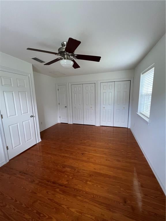 unfurnished bedroom with dark hardwood / wood-style floors, two closets, and ceiling fan