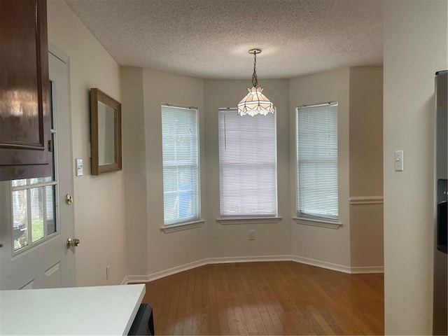 unfurnished dining area featuring a wealth of natural light, wood-type flooring, and a textured ceiling