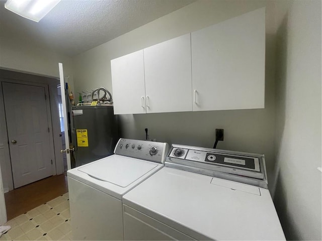 washroom with a textured ceiling, water heater, cabinets, light hardwood / wood-style floors, and washing machine and dryer