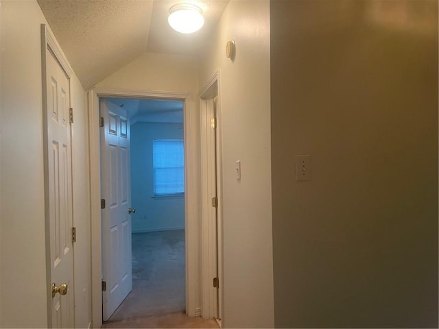 corridor featuring lofted ceiling, a textured ceiling, and light colored carpet