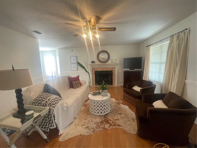 living room with hardwood / wood-style floors, a tile fireplace, ceiling fan, and a textured ceiling