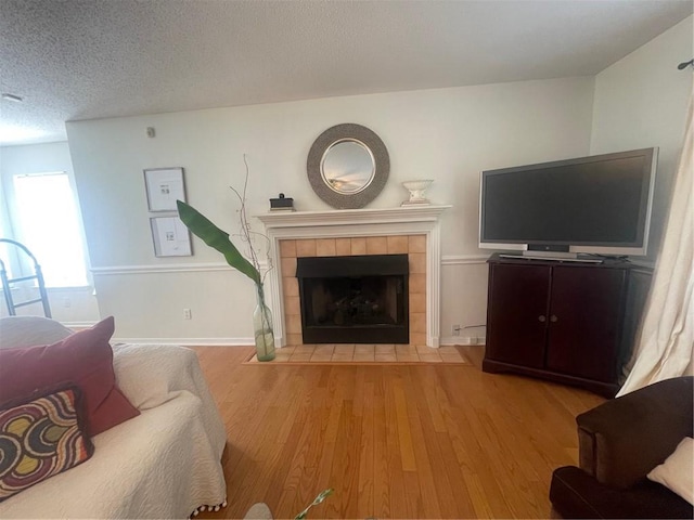 living room featuring a tiled fireplace, a textured ceiling, and light hardwood / wood-style flooring