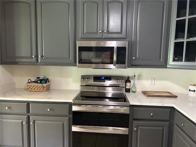 kitchen featuring gray cabinetry, stainless steel appliances, and light stone counters