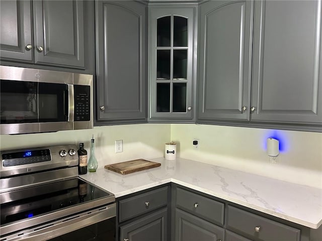 kitchen featuring light stone countertops, stainless steel appliances, and gray cabinetry