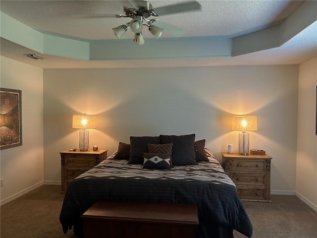 bedroom featuring a textured ceiling, a tray ceiling, dark carpet, and ceiling fan