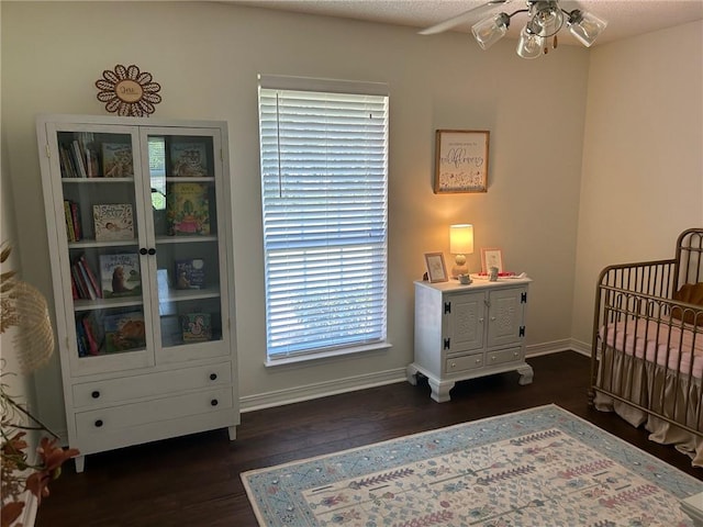 bedroom featuring a textured ceiling, dark wood-type flooring, ceiling fan, and a nursery area