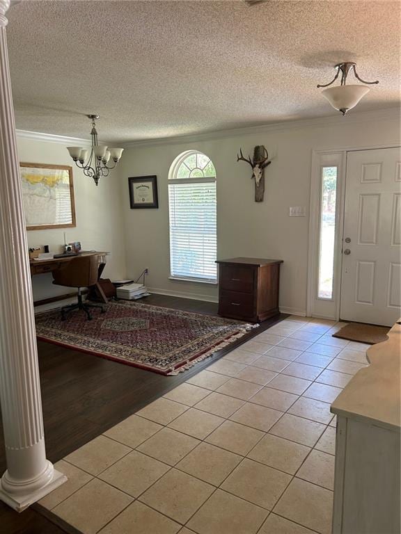 tiled foyer featuring a textured ceiling, crown molding, decorative columns, and a chandelier