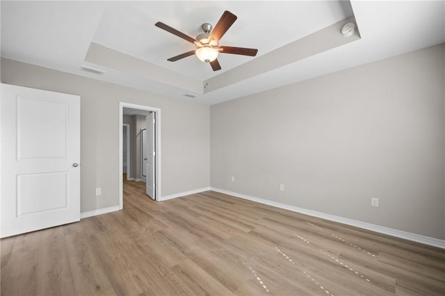 unfurnished bedroom with ceiling fan, a tray ceiling, and light hardwood / wood-style flooring