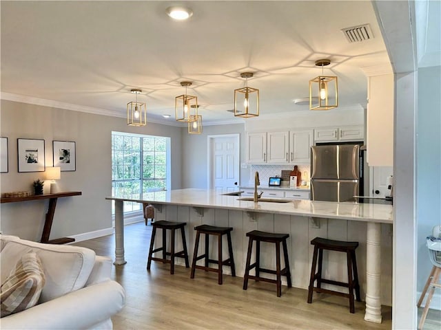 kitchen featuring visible vents, a kitchen bar, freestanding refrigerator, and crown molding