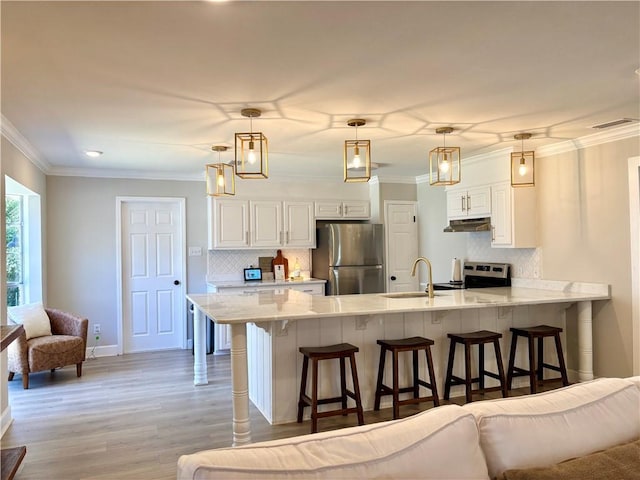 kitchen featuring appliances with stainless steel finishes, open floor plan, a peninsula, under cabinet range hood, and a kitchen bar